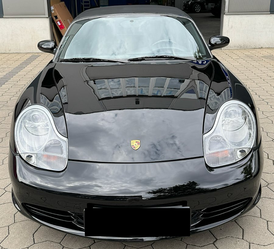 Front des schwarzen Porsche Boxster S, in der Motorhaube spiegelt sich die CARFIT-Halle