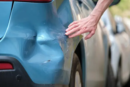 Bild zeigt erhebliche Dellen in der Vorderschürze und dem linken Kotflügel eines blau-metallic Fahrzeugs